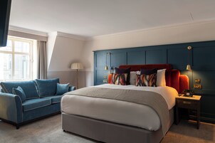 Ein modernes Schlafzimmer mit einem großen Bett, einem blauen Sofa und einem Nachttisch mit Lampe.
