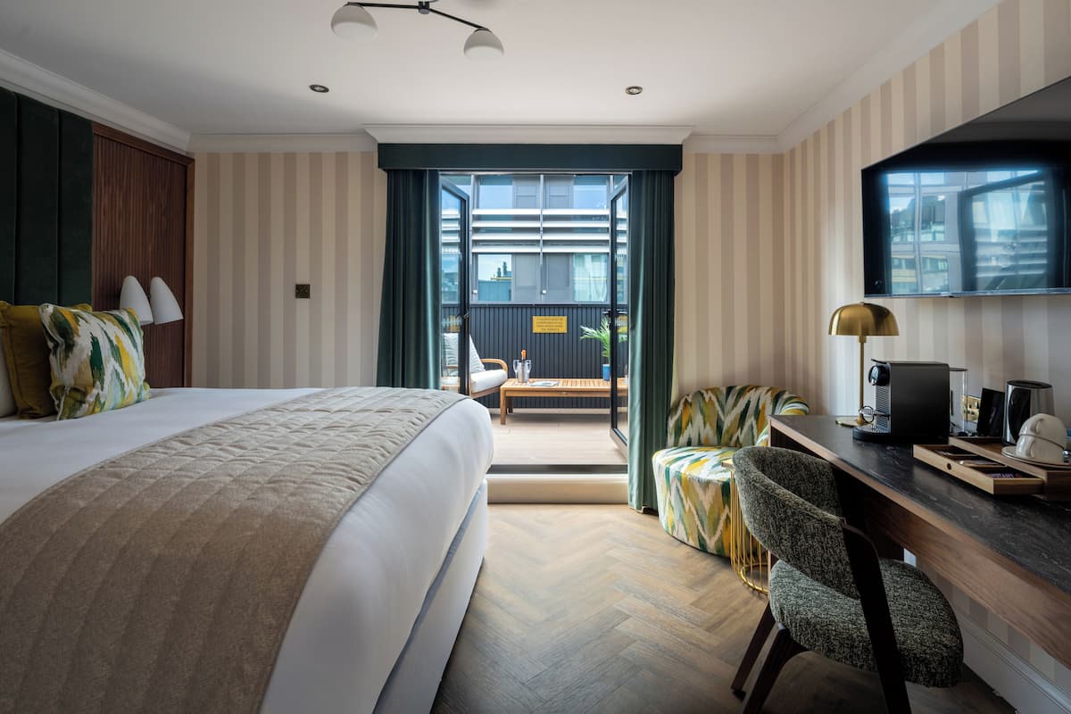 Quarto de hotel moderno com uma cama grande, uma mesa com computador, uma cadeira e vista para a varanda externa.