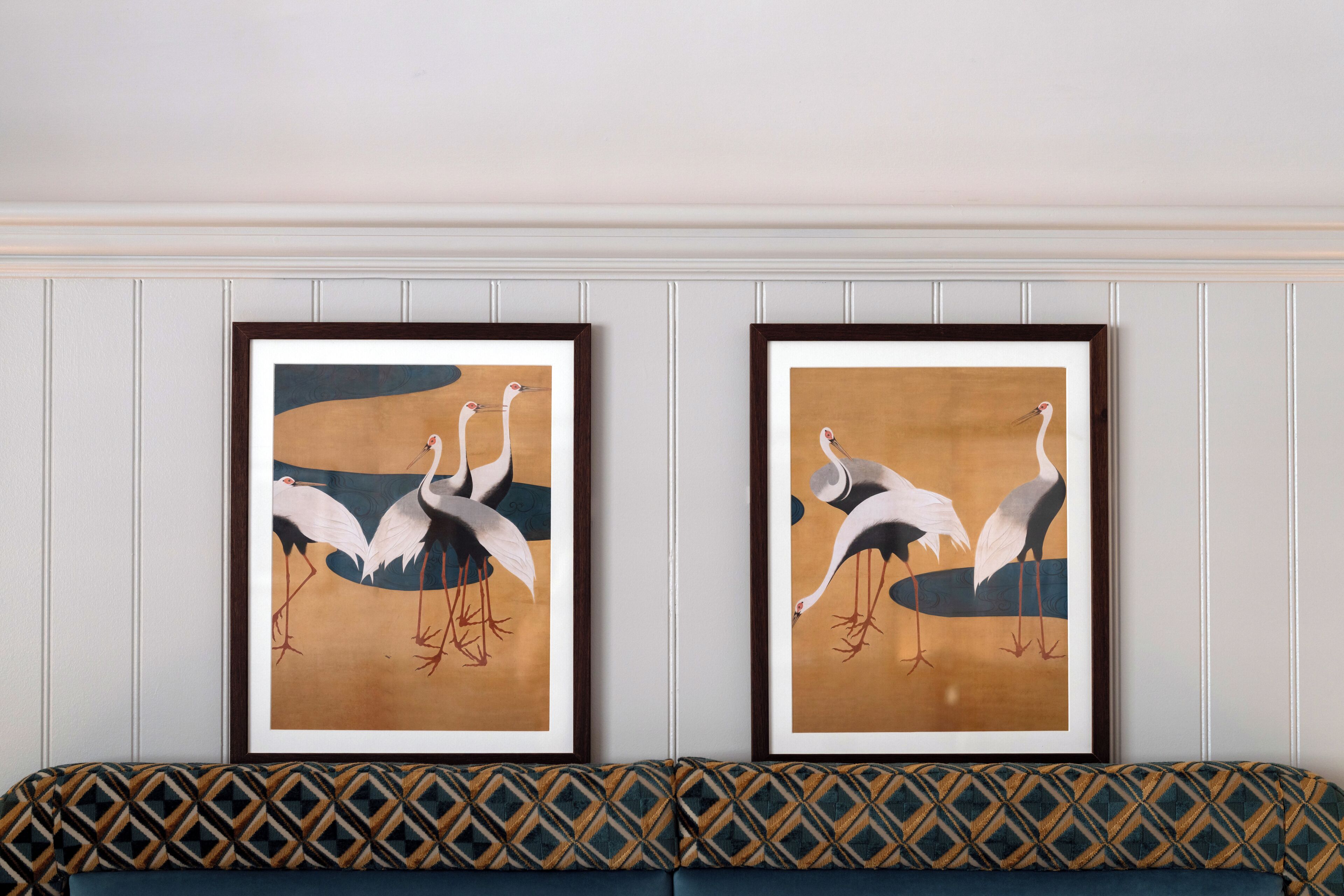 Two framed artworks of birds on a wall above a patterned sofa.