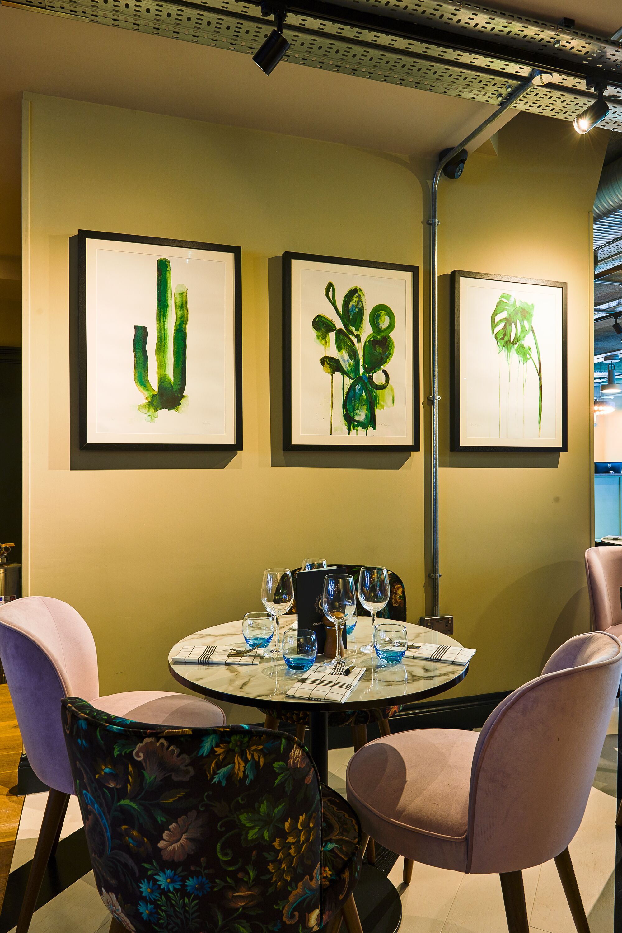 Un coin repas avec une table ronde dressée pour deux personnes, des œuvres d’art encadrées au mur et des chaises modernes.