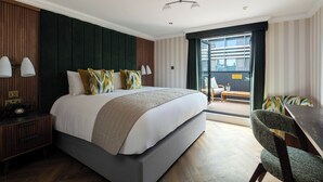 A modern hotel room with a large bed, a desk, and a chair. There is a window with a view of the city. - The Chamberlain Hotel (London)