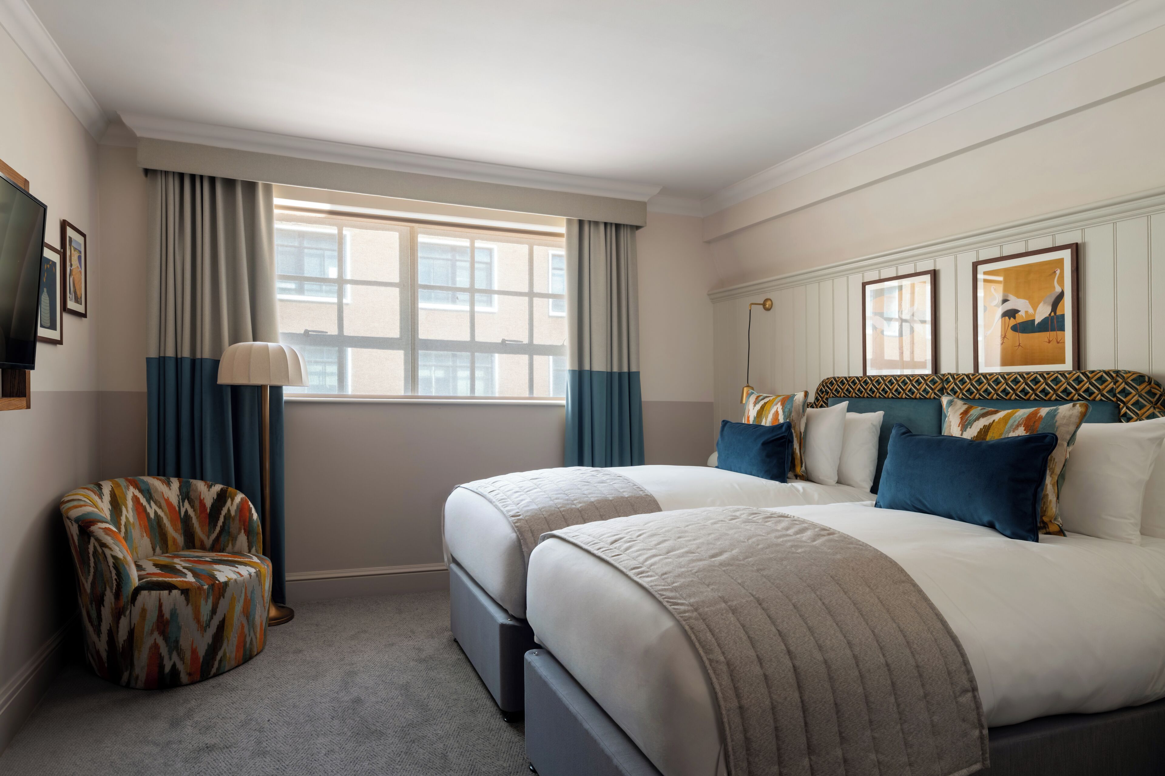 Quarto de hotel com duas camas, uma cadeira, uma televisão e uma janela com cortinas.