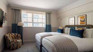 Quarto de hotel com duas camas, uma cadeira, uma televisão e uma janela com cortinas.