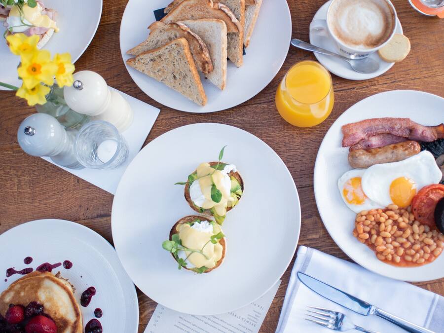 A breakfast table with various dishes including toast, eggs, sausages, and pancakes.