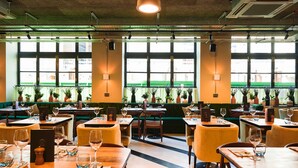 A restaurant with multiple tables and booths, large windows with a view of the street, and indoor plants. - The Chamberlain Hotel (London)