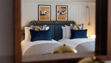 A hotel room with a bed, two framed artworks on the wall, a patterned headboard, and a bedside lamp.