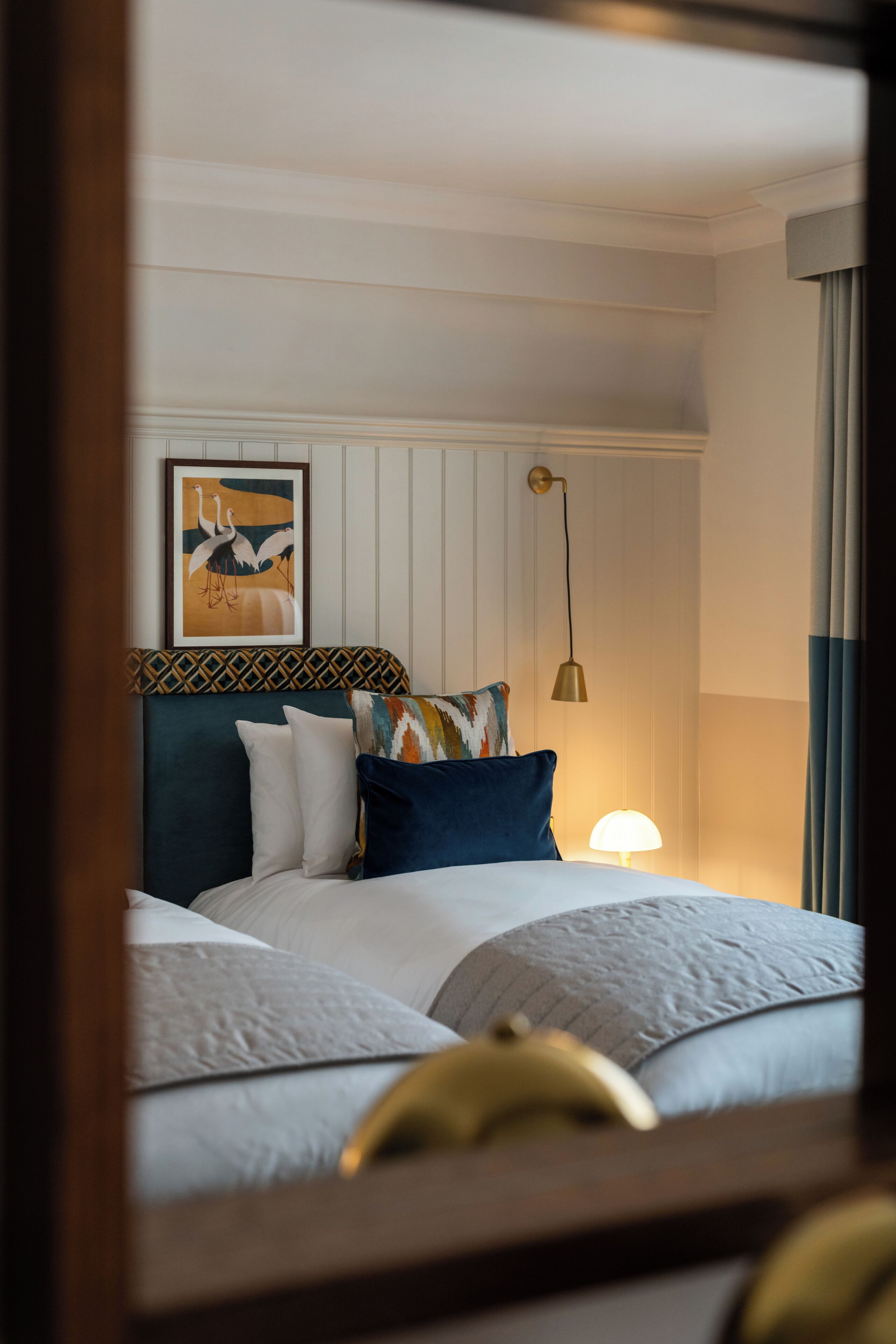A neatly made bed with multiple pillows, a wall-mounted lamp, and a framed picture above the bed.