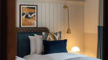 A neatly made bed with multiple pillows, a wall-mounted lamp, and a framed picture above the bed.