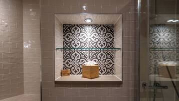 Un baño con baldosas color beige, una pared decorativa con azulejos blanco y negro, un caja de madera y una estantería de vidrio.