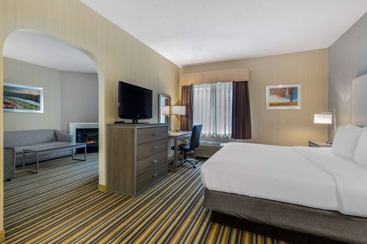 A hotel room with a bed, a desk, a television, a sofa, and a fireplace.