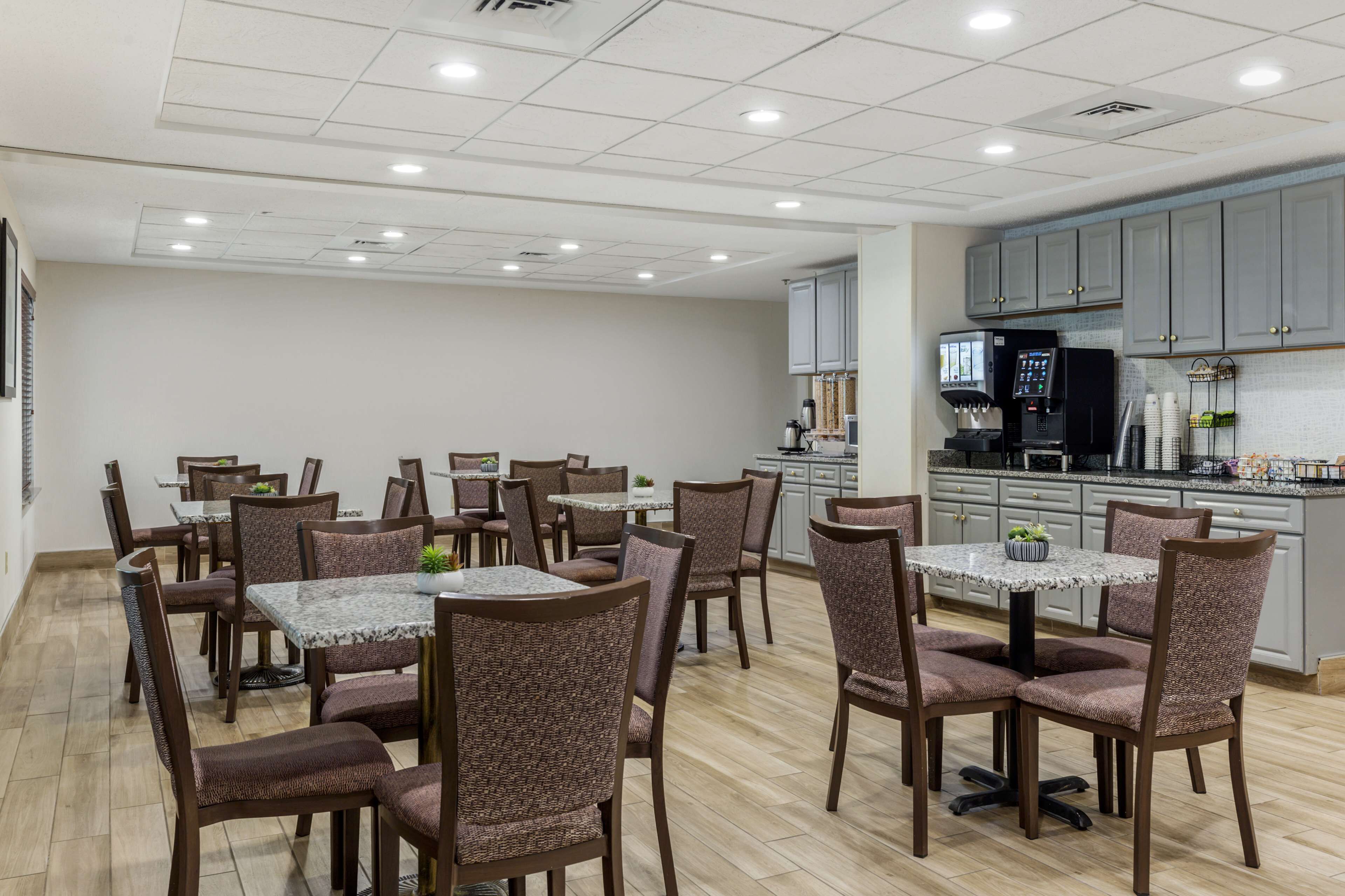 A dining area with multiple tables and chairs, a kitchen area with cabinets and appliances, and a tiled floor.