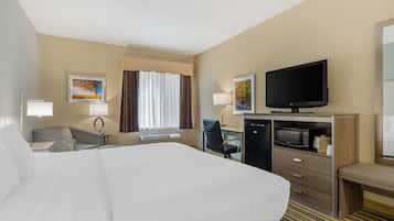 A hotel room with a large bed, a desk with a computer, a television, a microwave, and a seating area.