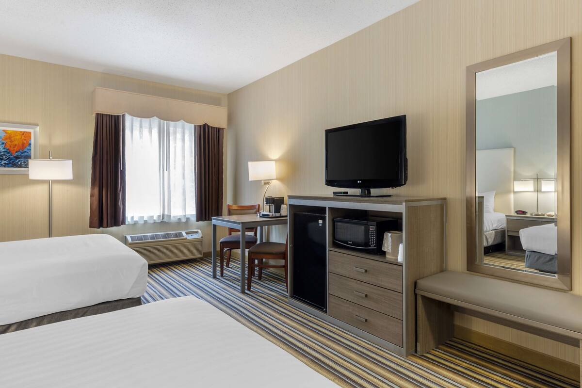 A hotel room with two beds, a desk with a television, a microwave, and a large mirror.