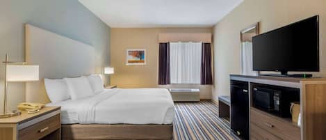 Ein Hotelzimmer mit Bett, Nachttisch mit Lampe, Telefon, Flachbildfernseher, Mikrowelle und einem Streifenmuster-Teppich.