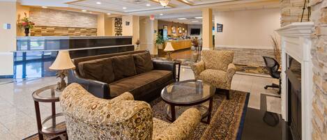 A lobby with a sofa, armchairs, a coffee table, a fireplace, a reception desk, and a stone wall.