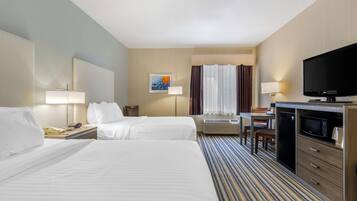 A hotel room with two beds, a desk with a television, a microwave, and a window with curtains.