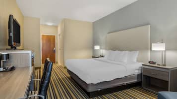 A hotel room with a bed, bedside tables, a desk with a chair, a television, and a door leading to another room.