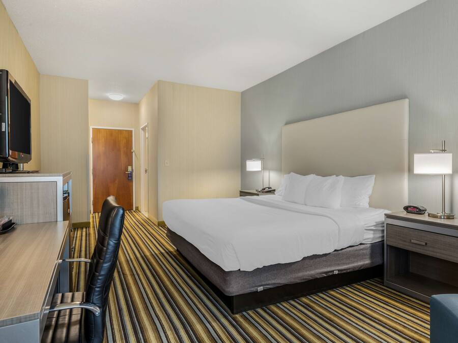 Une chambre d’hôtel comprenant un lit, des tables de chevet, un bureau avec une chaise, une télévision et une porte donnant sur une autre pièce.
