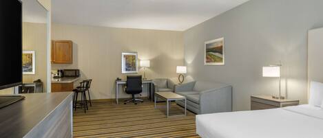 A hotel room with a bed, a desk with a chair, a sofa, a TV, a microwave, and a lamp.