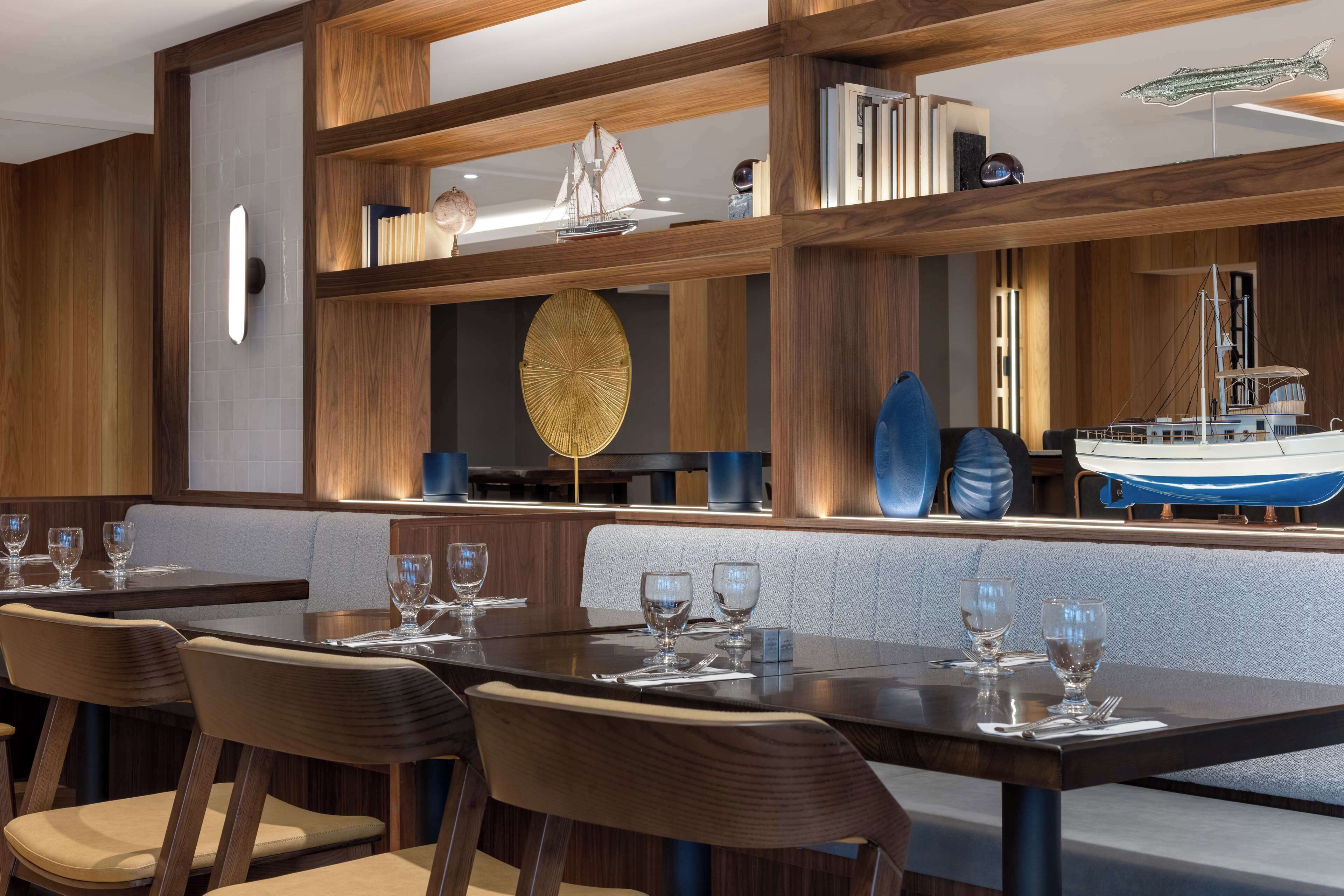 A restaurant with wooden paneling, a central seating area with tables and chairs, and a bar area with a model ship display.