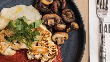 A plate with mashed potatoes, grilled mushrooms, and a red sauce, accompanied by a fork and napkin on a wooden table.