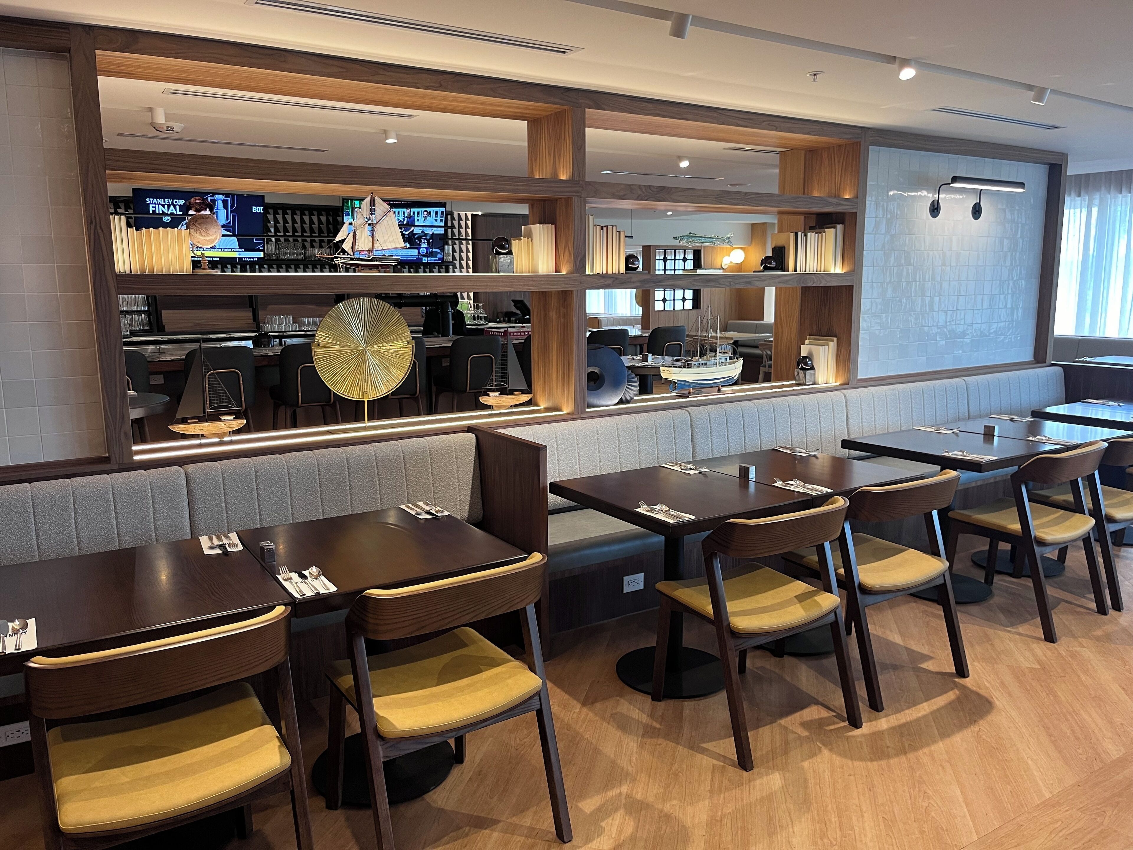 Un restaurante con mesas y cabinas de madera, una zona de bar con pantalla de televisión y un modelo decorativo de velero.