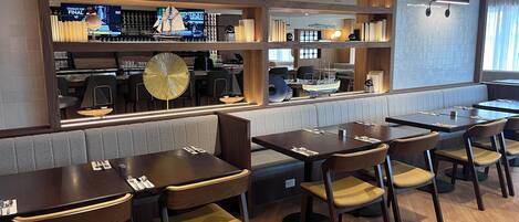 Un restaurante con mesas y cabinas de madera, una zona de bar con pantalla de televisión y un modelo decorativo de velero.