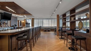 A spacious bar area with multiple seating options, a long counter, and a modern design with wooden accents and a large window providing natural light. - DoubleTree by Hilton Kingston (Kingston)