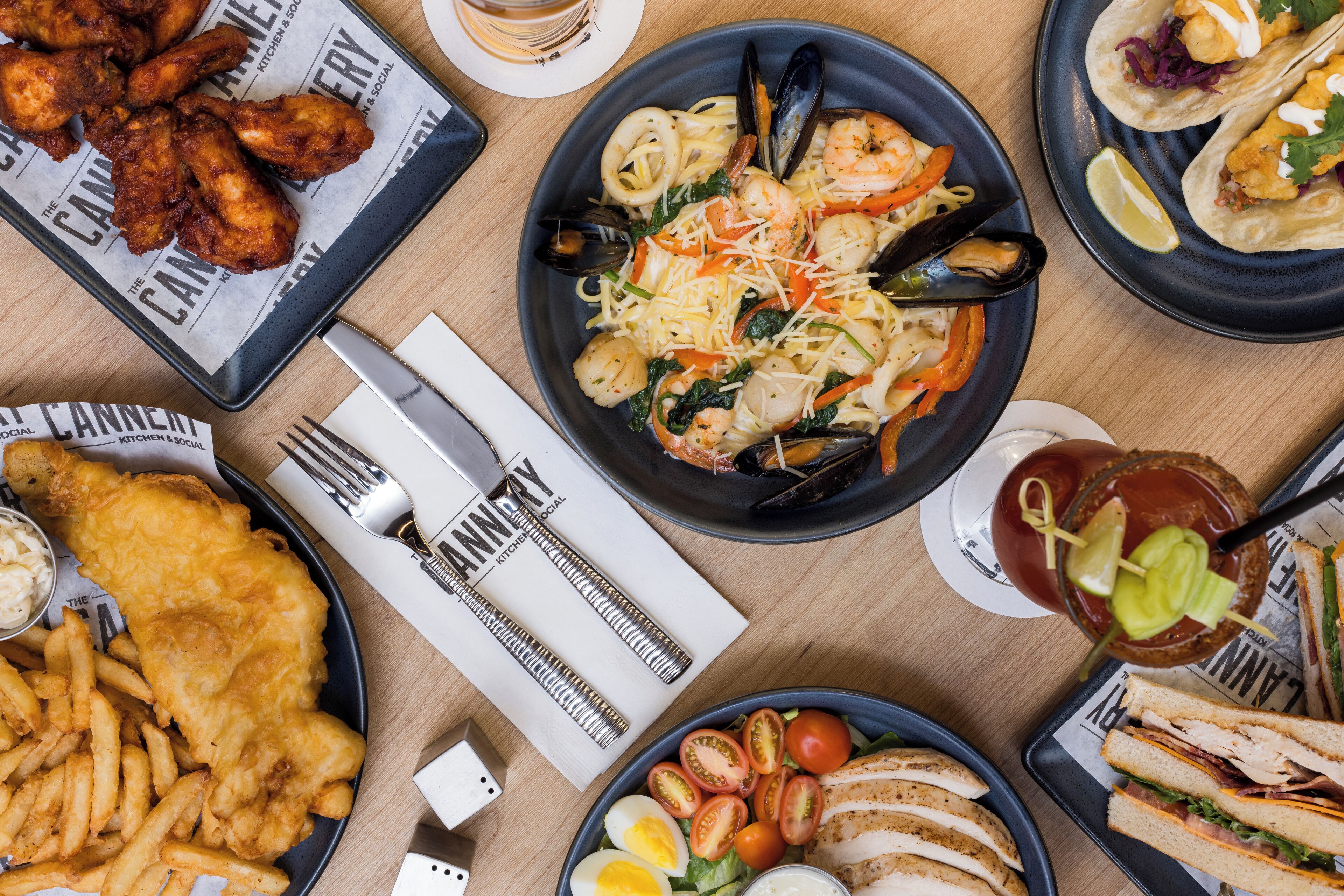 Verschiedene Gerichte, darunter Meeresfrüchte-Pasta, Fish and Chips sowie Sandwiches, stehen auf einem Tisch.