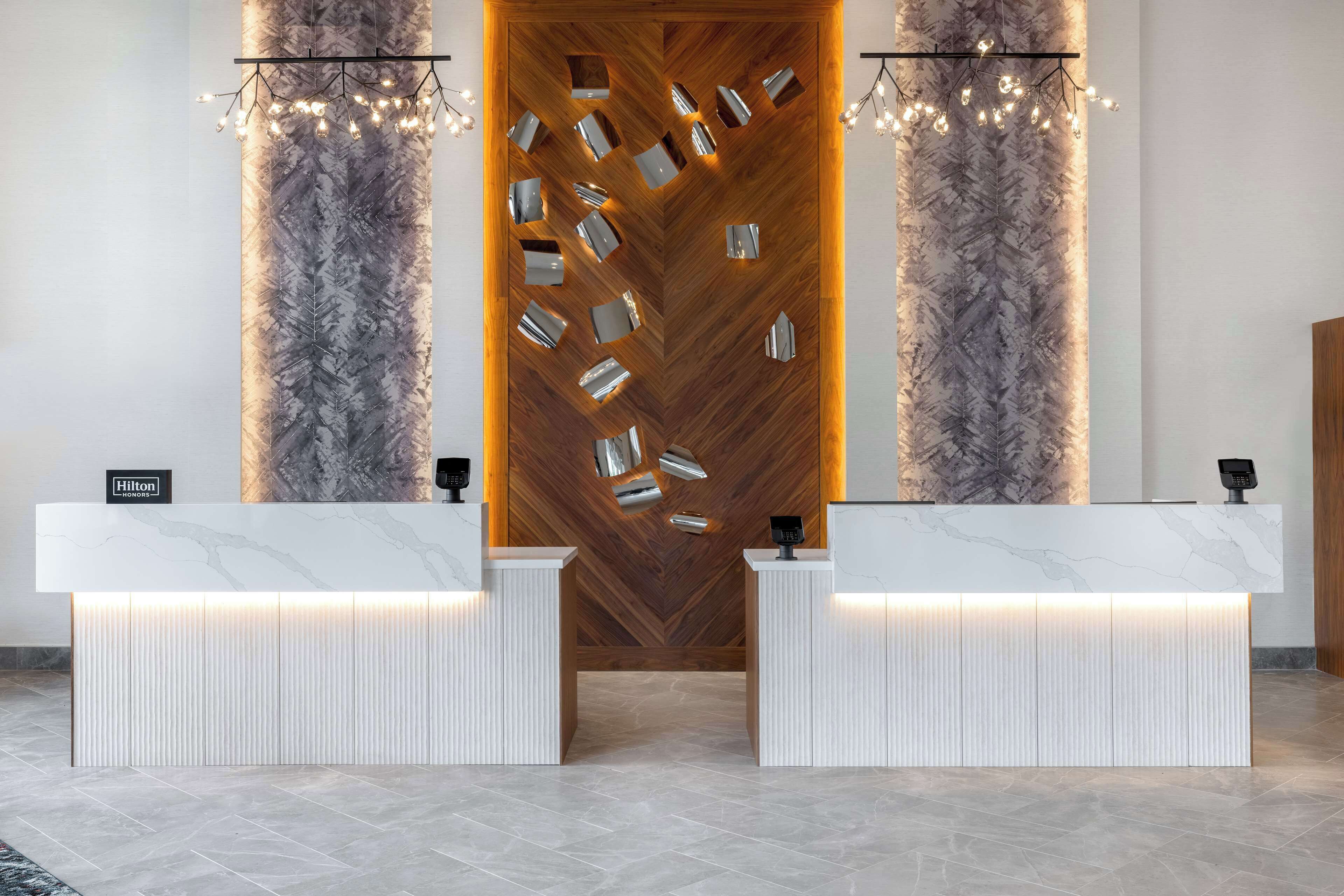 En hotellobby med modern design, med en receptionsdisk i marmor, en vägg med trädetaljer och en kristallkrona.