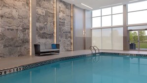 A modern indoor swimming pool with a stone wall, a lounge area with a sofa, and large windows. - DoubleTree by Hilton Kingston (Kingston)