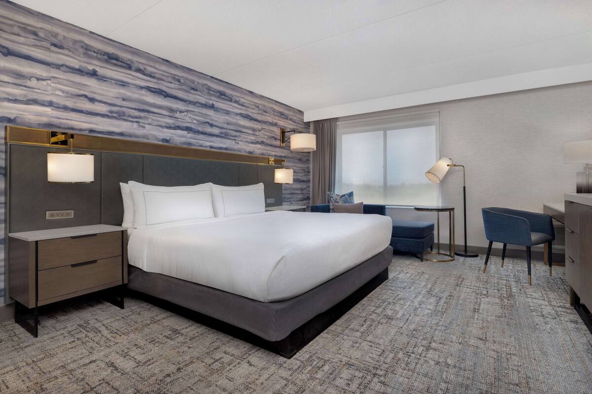 A modern hotel room with a large bed, a desk, and a chair.