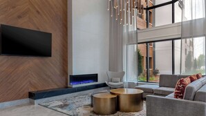 A modern living room with a fireplace, a flat-screen TV mounted on the wall, and a large window offering a view of the outdoors. - DoubleTree by Hilton Kingston (Kingston)
