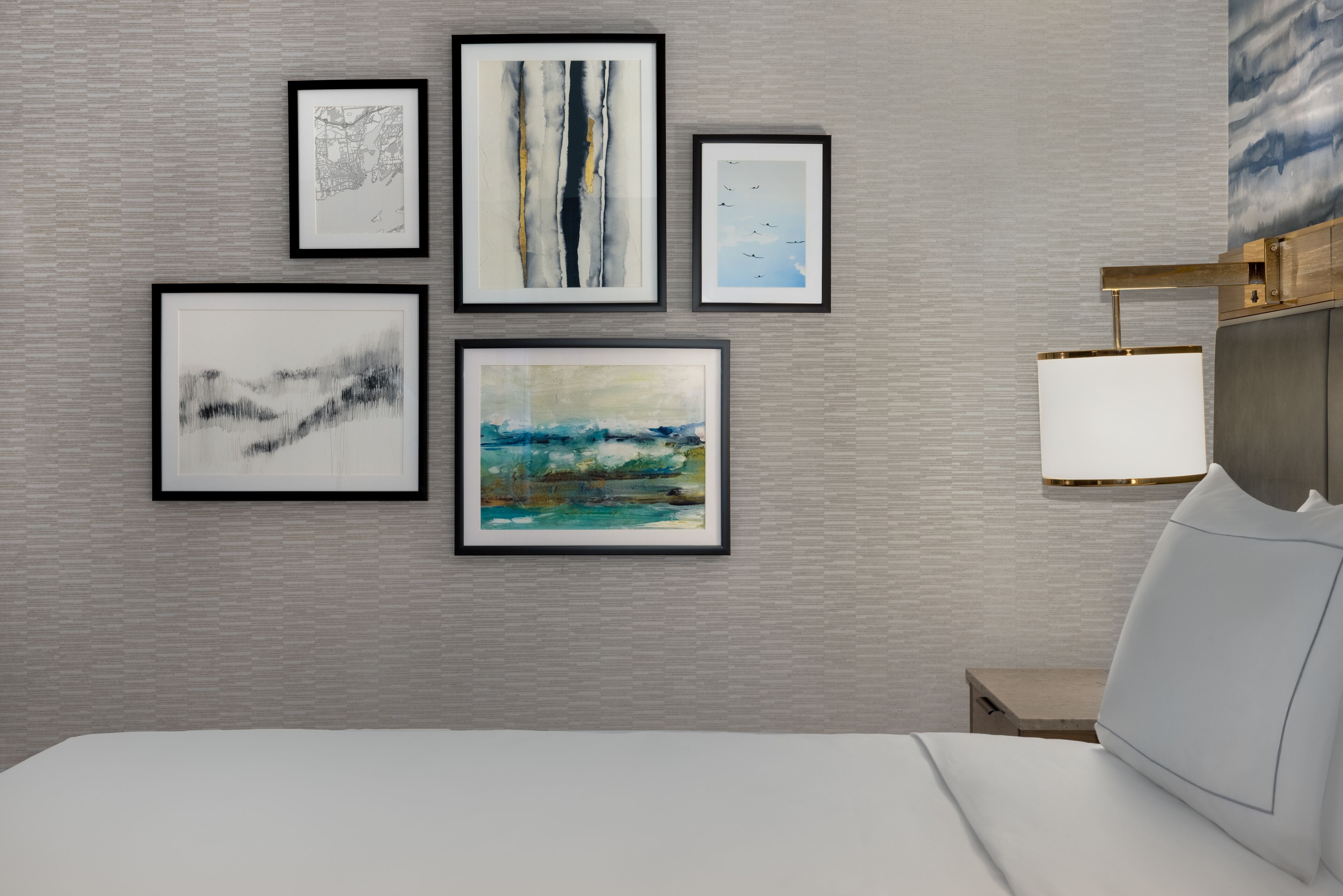 A hotel room with a bed, a nightstand, and a wall with five framed artworks.
