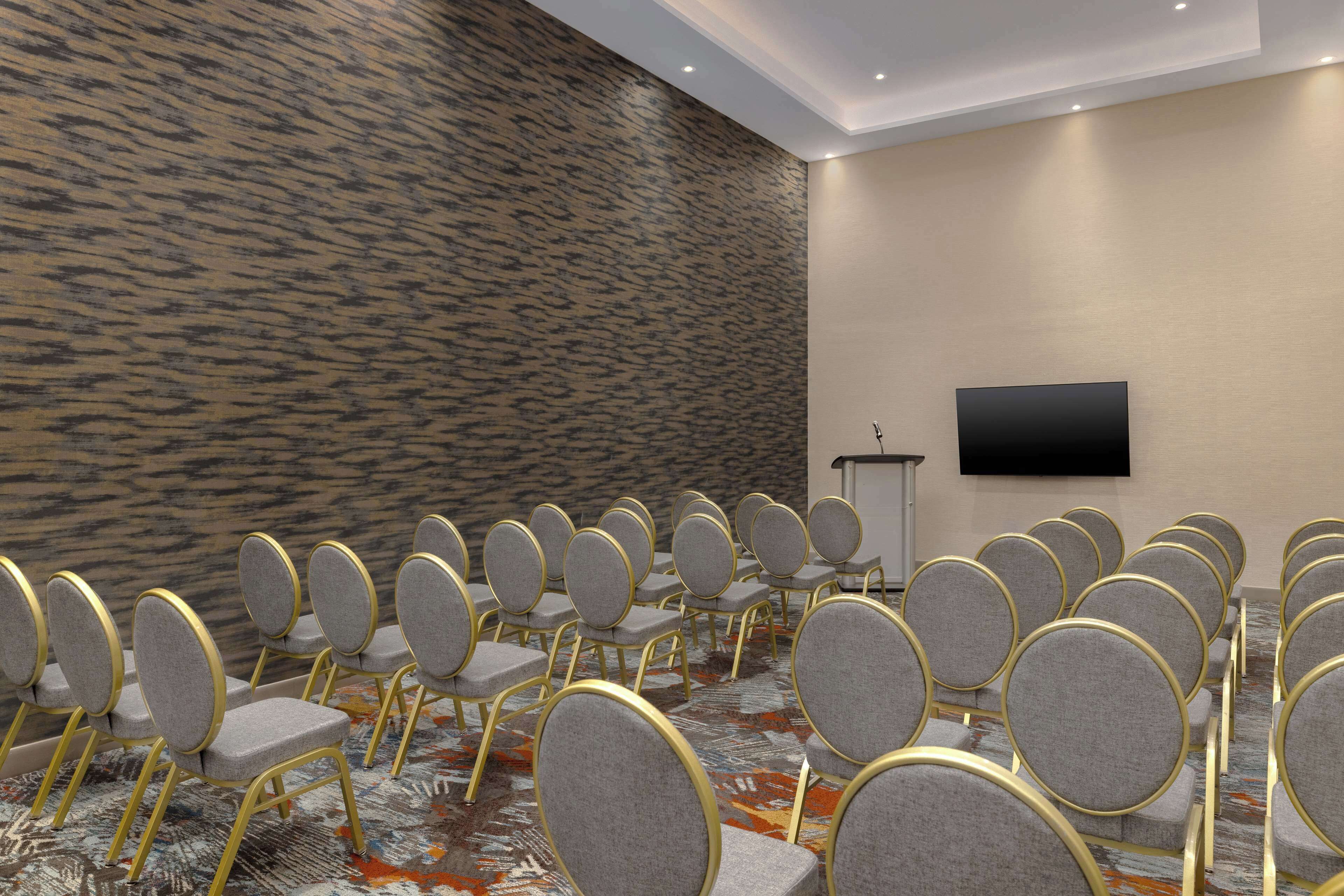 A conference room with rows of grey chairs and a flat-screen TV mounted on the wall.