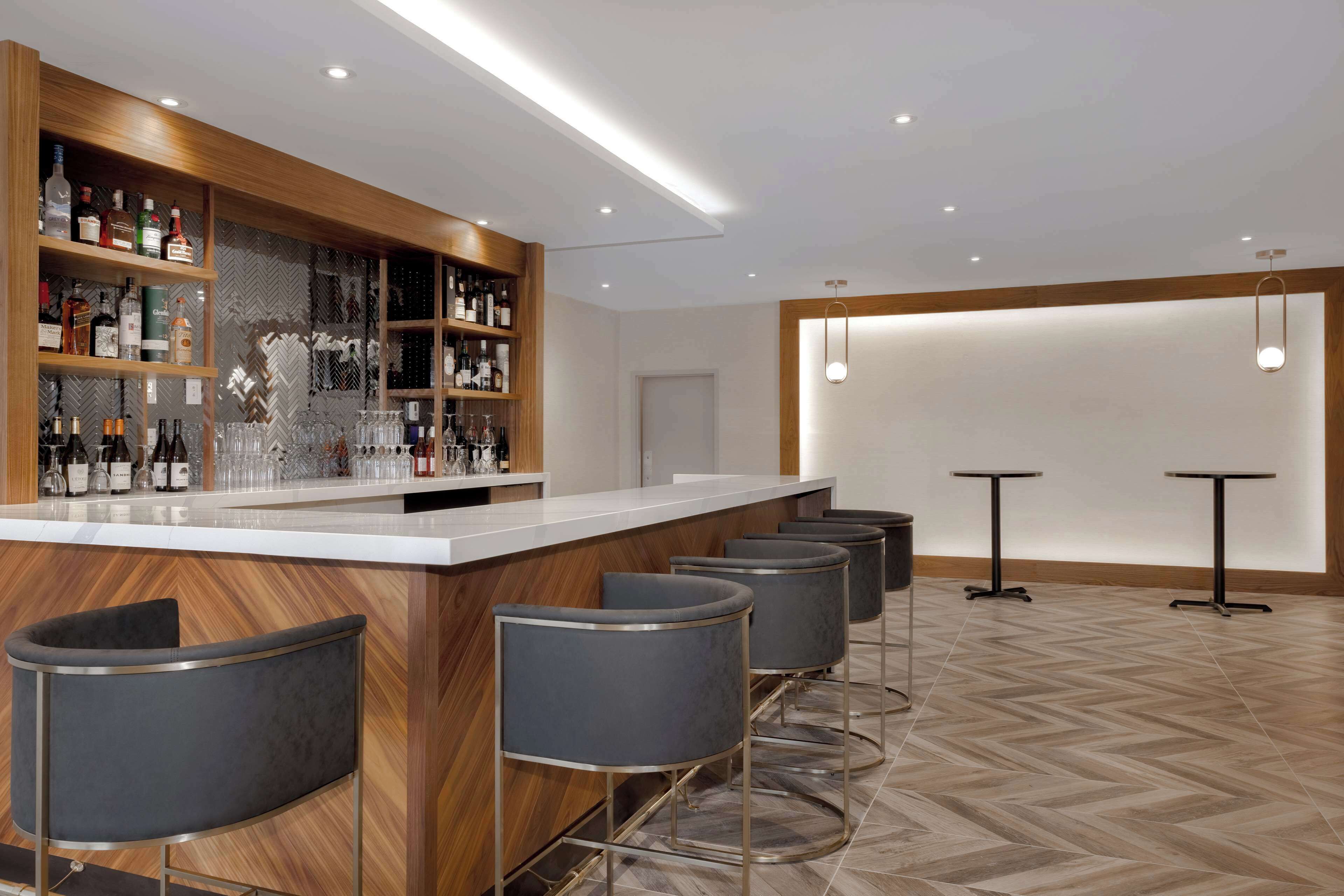 Un espace bar moderne, doté d’un comptoir en bois, de plusieurs tabourets et d’une variété de bouteilles et de verres.