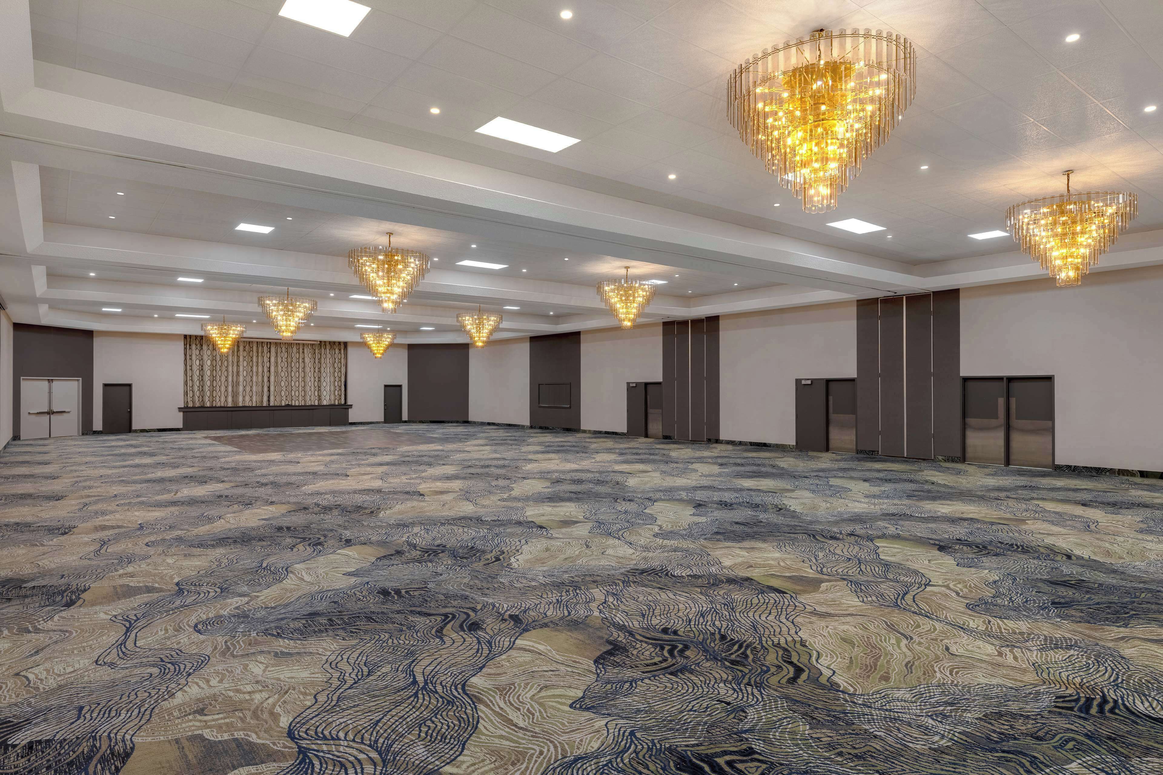 A spacious conference room with patterned carpet, multiple chandeliers, and a neutral color scheme.