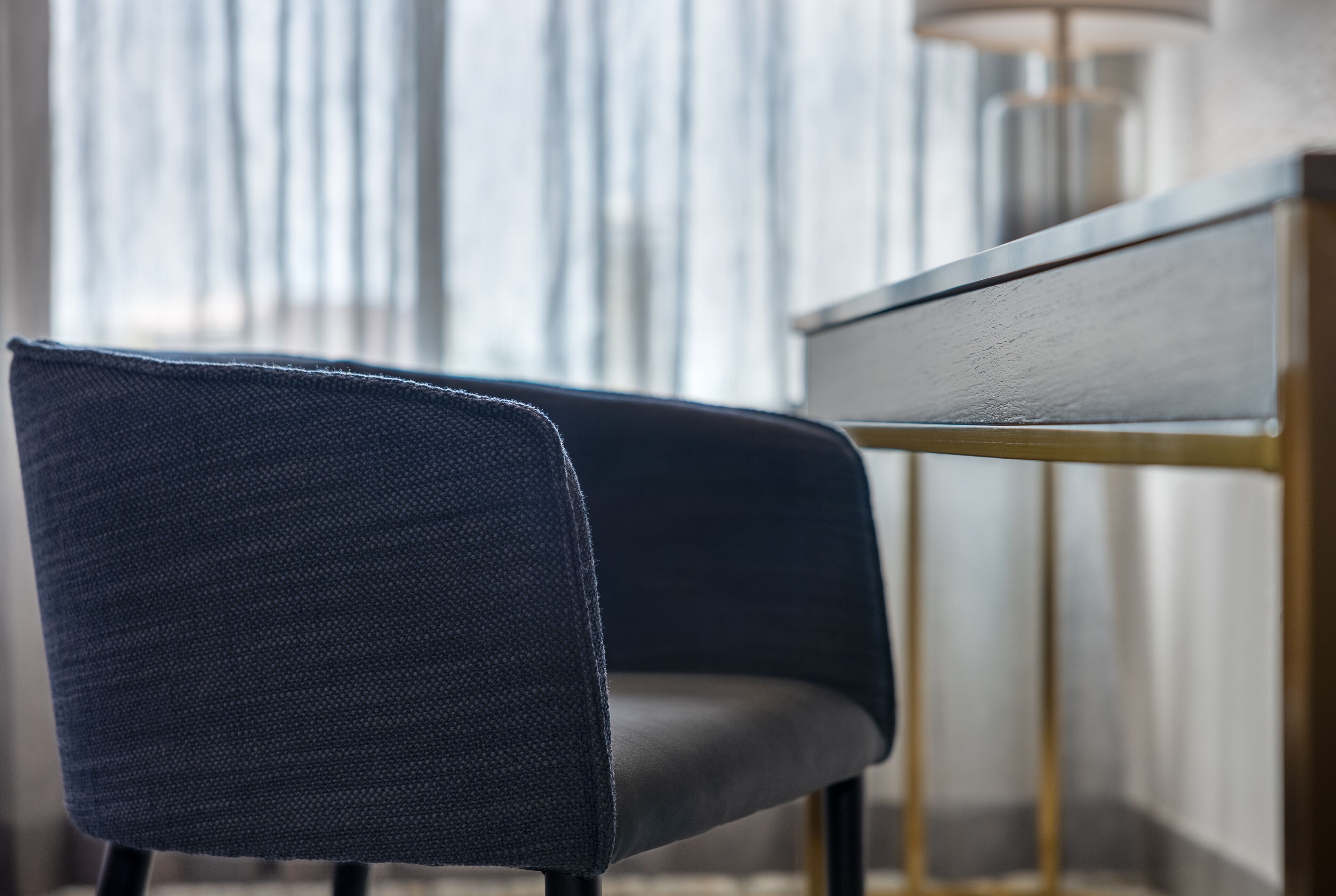 Una silla moderna con tela oscura y una mesa de madera con marco dorado.