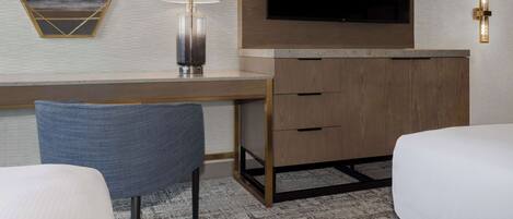 Een hotelkamer met een houten bureau, een flatscreen televisie erboven, een moderne lamp en een grote spiegel met een geometrisch lijstwerk.