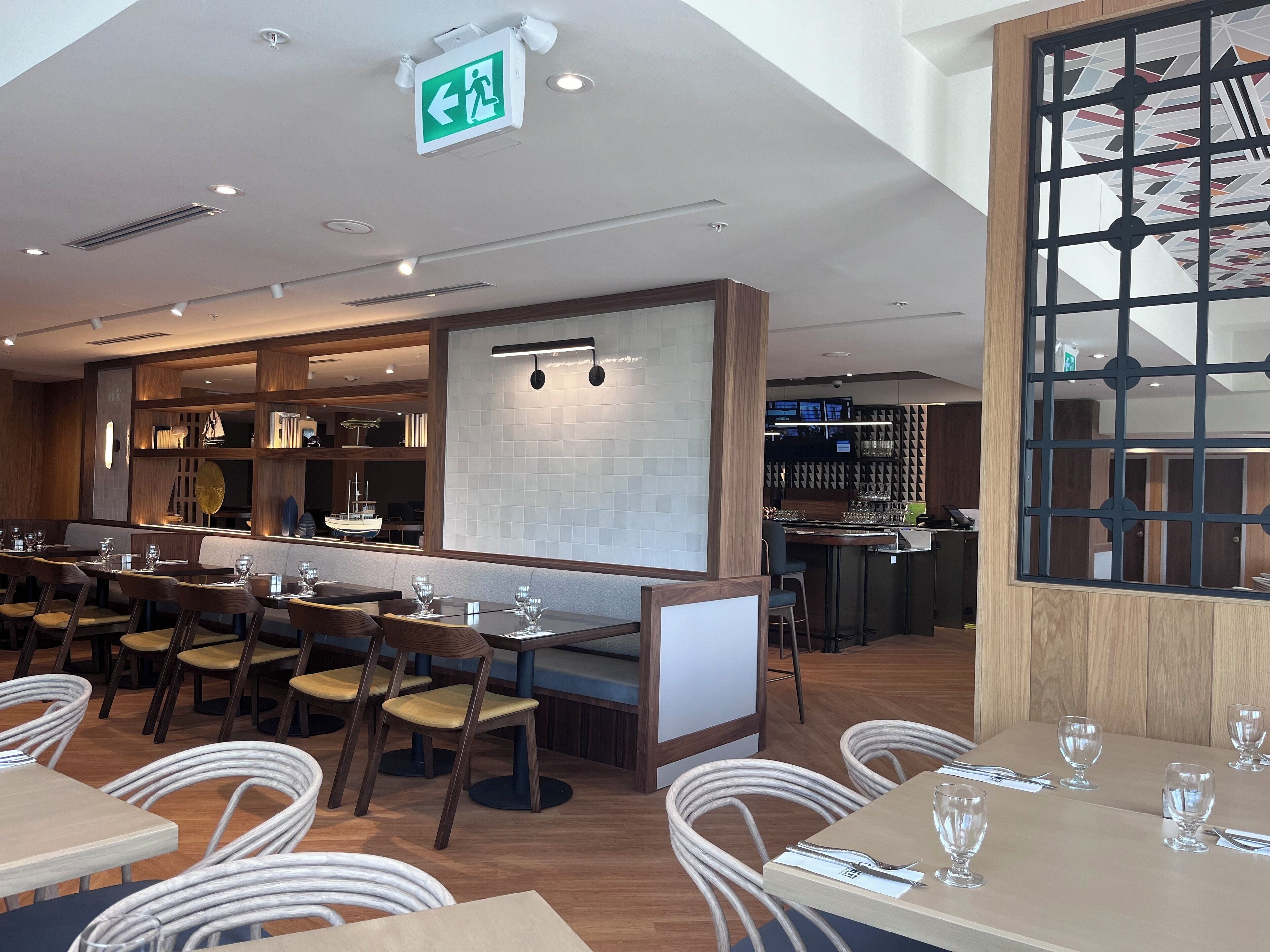 En restaurang med en bardel, sittplatser och en tydligt markerad nödutgång.