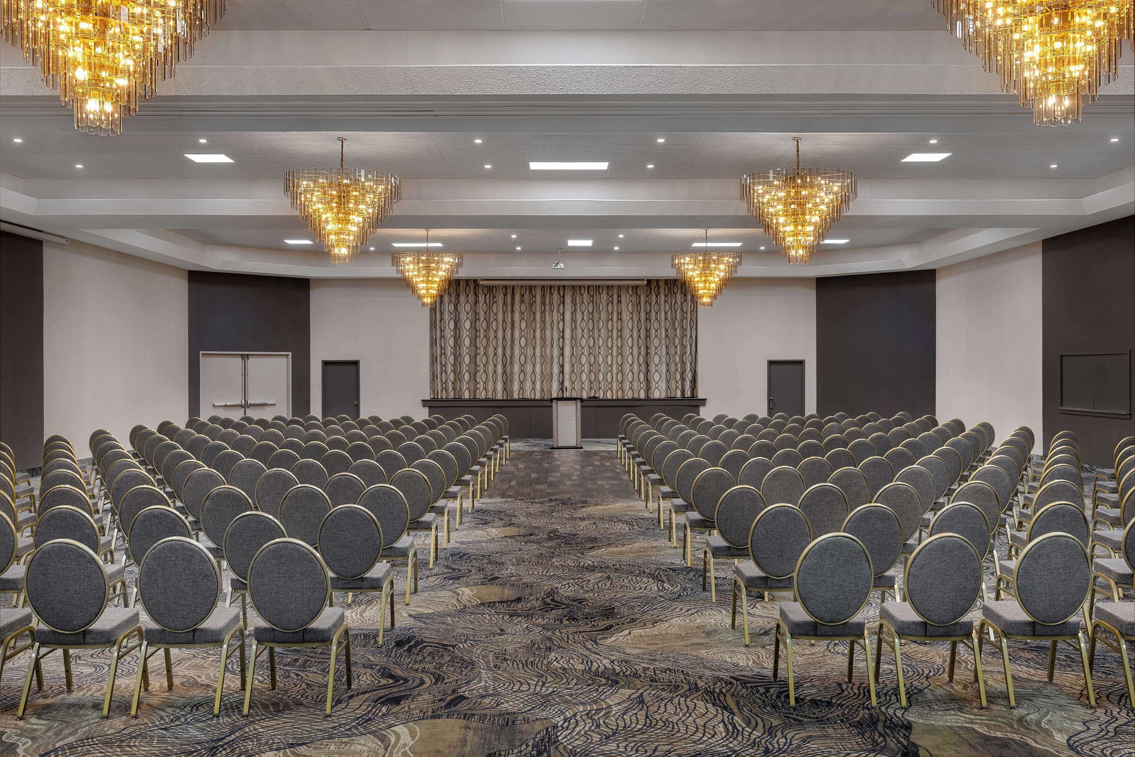Un salón de conferencias con filas de sillas, una alfombra estampada y candelabros.