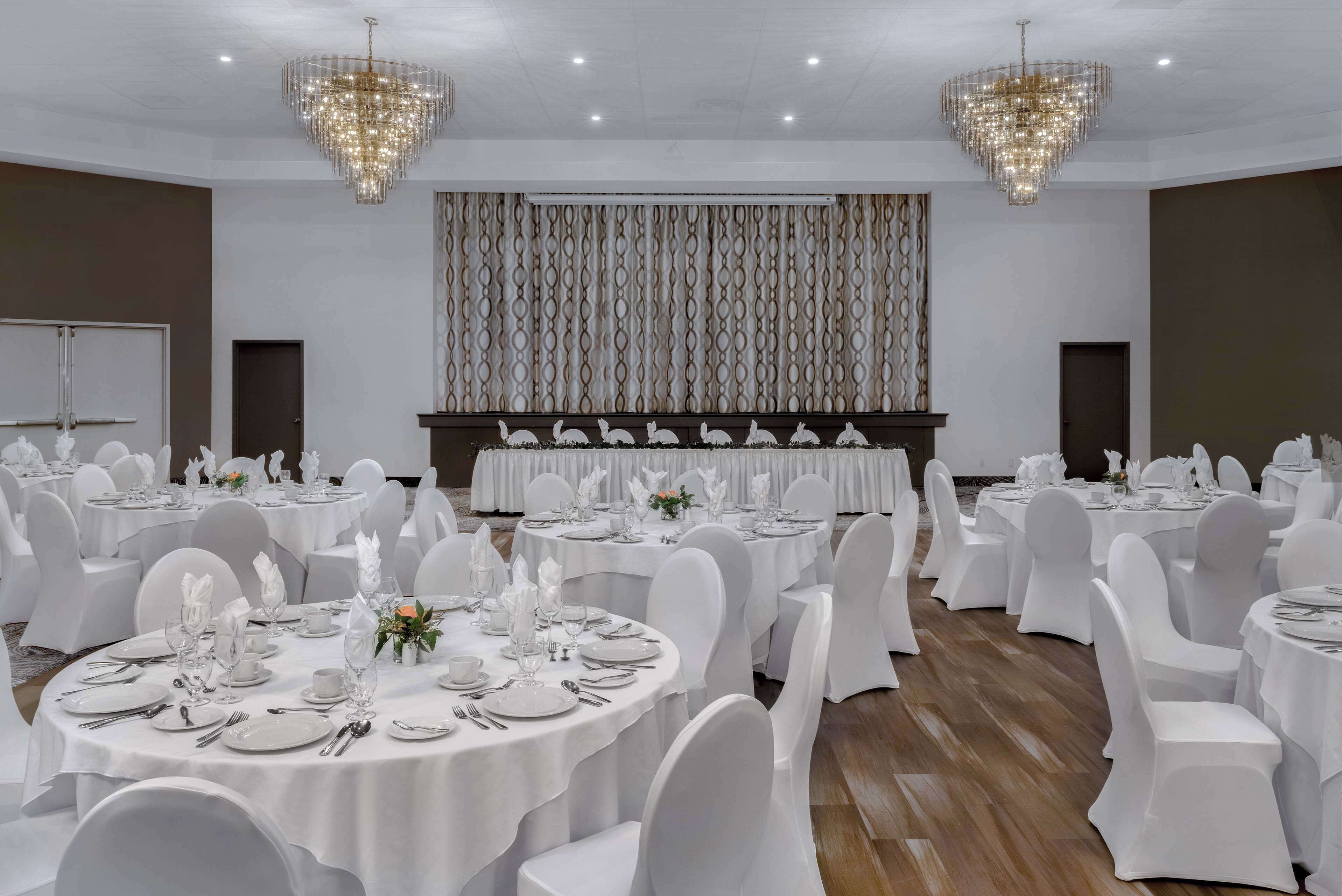 A banquet hall with round tables, white chairs, and chandeliers.