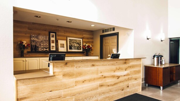 Un mostrador de recepción con detalles de madera, obras de arte enmarcadas en la pared, una computadora portátil sobre el mostrador y una estación de café a la derecha.