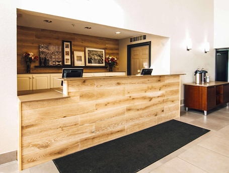 A reception desk with a wooden finish, framed artwork on the wall, a laptop on the desk, and a coffee station to the right.. Country Inn & Suites by Radisson, Stockton, IL