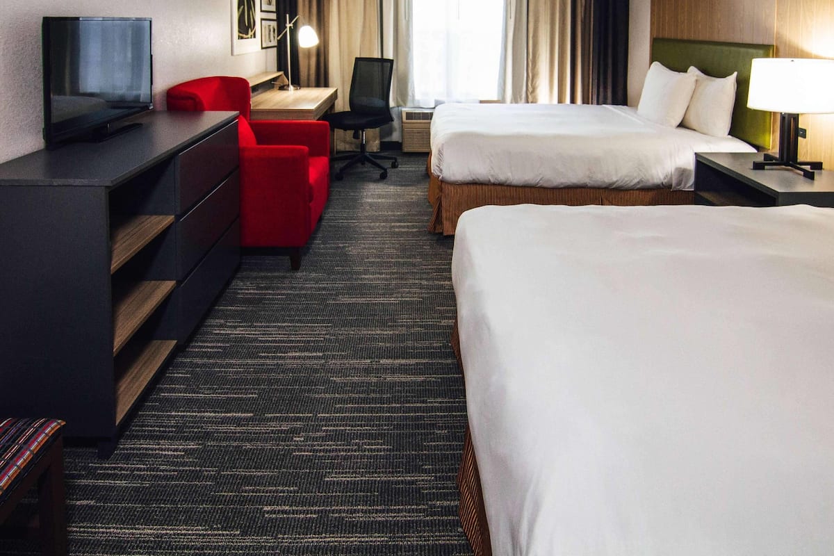 A hotel room with two beds, a desk with a chair, a TV, and a red armchair.