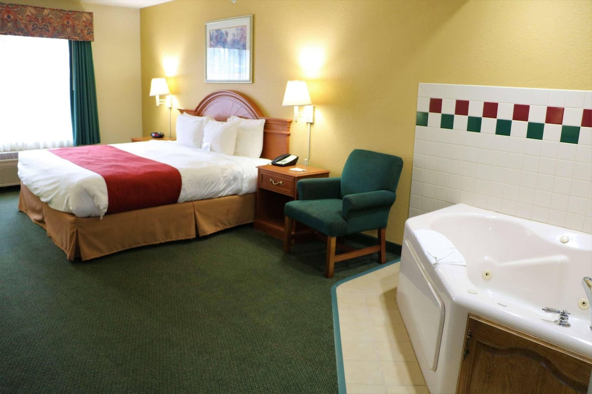 A hotel room with a bed, a chair, a desk with a lamp, a telephone, and a bathtub.