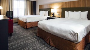 Habitación de hotel con dos camas, un escritorio, una silla y un ventanal con cortinas.
