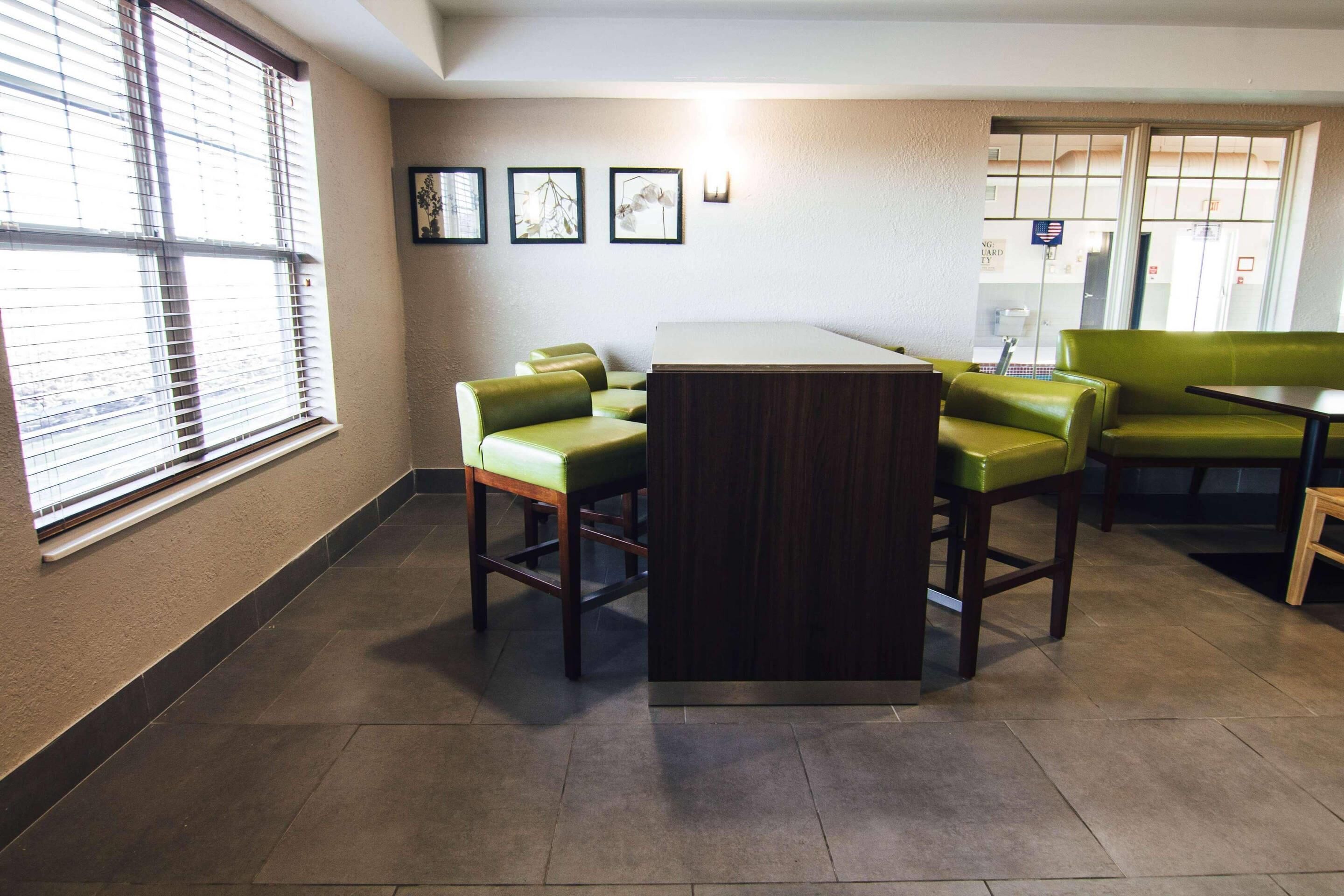 Une pièce comprenant un coin bar, des fauteuils à coussins verts, un comptoir de bar en bois et des tableaux encadrés accrochés au mur.