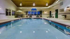 Una piscina interior con agua cristalina, techo de madera y vista al cielo nocturno a través de un ventanal grande.