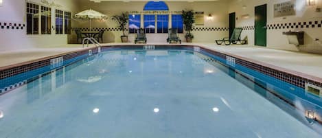 An indoor swimming pool with clear water, a wooden ceiling, and a view of the night sky through a large window.